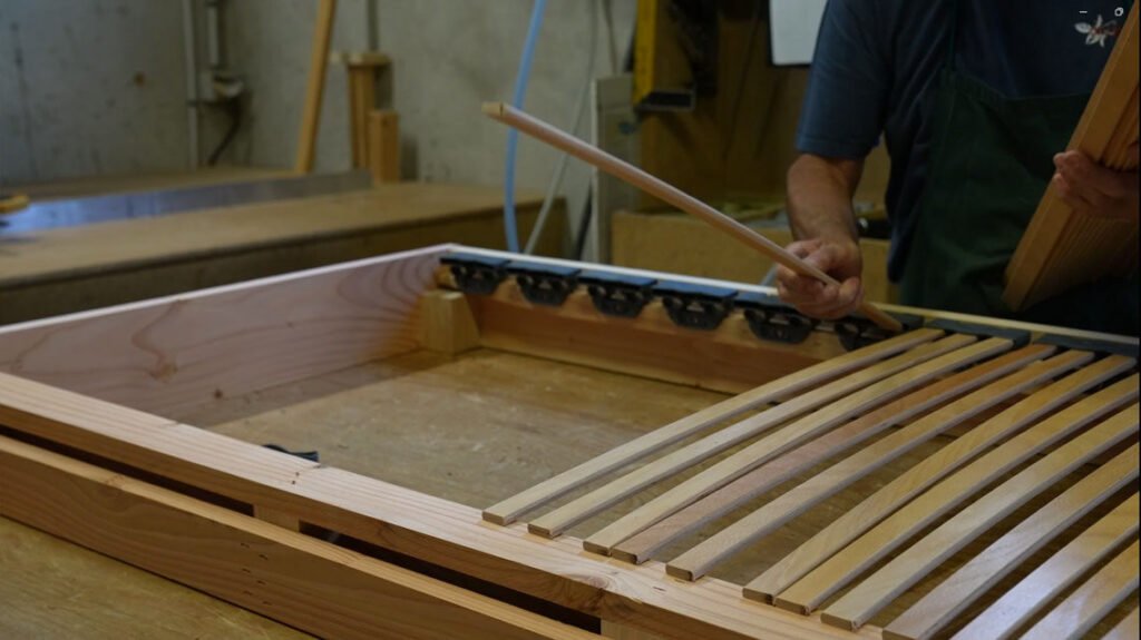 Pose des lattes en bois sur un sommier tapissier fabriqué en France dans l'atelier OX Literie