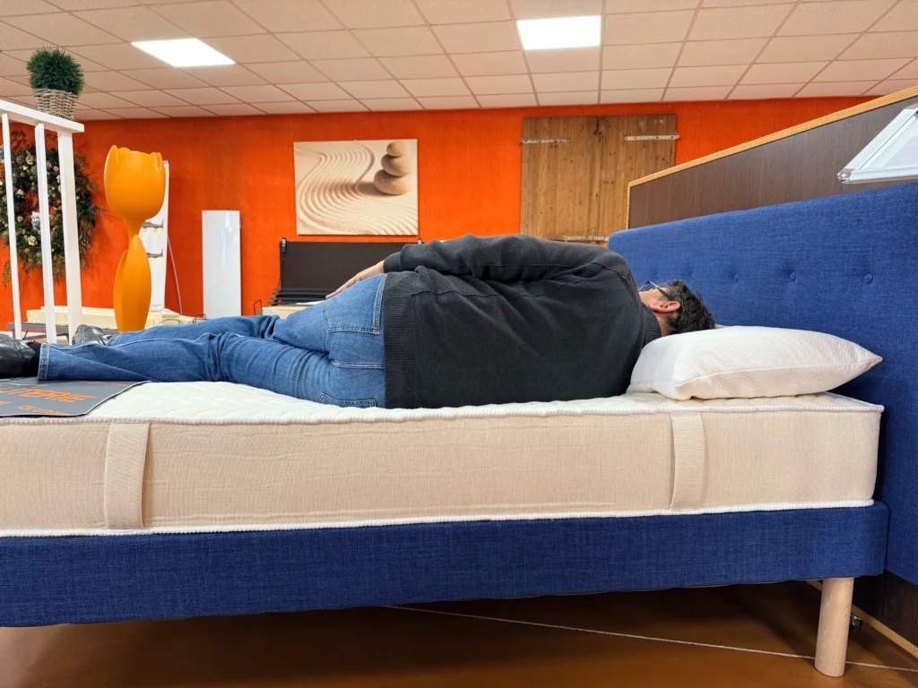 Client testant un matelas sur le côté en magasin OX LITERIE pour vérifier le confort